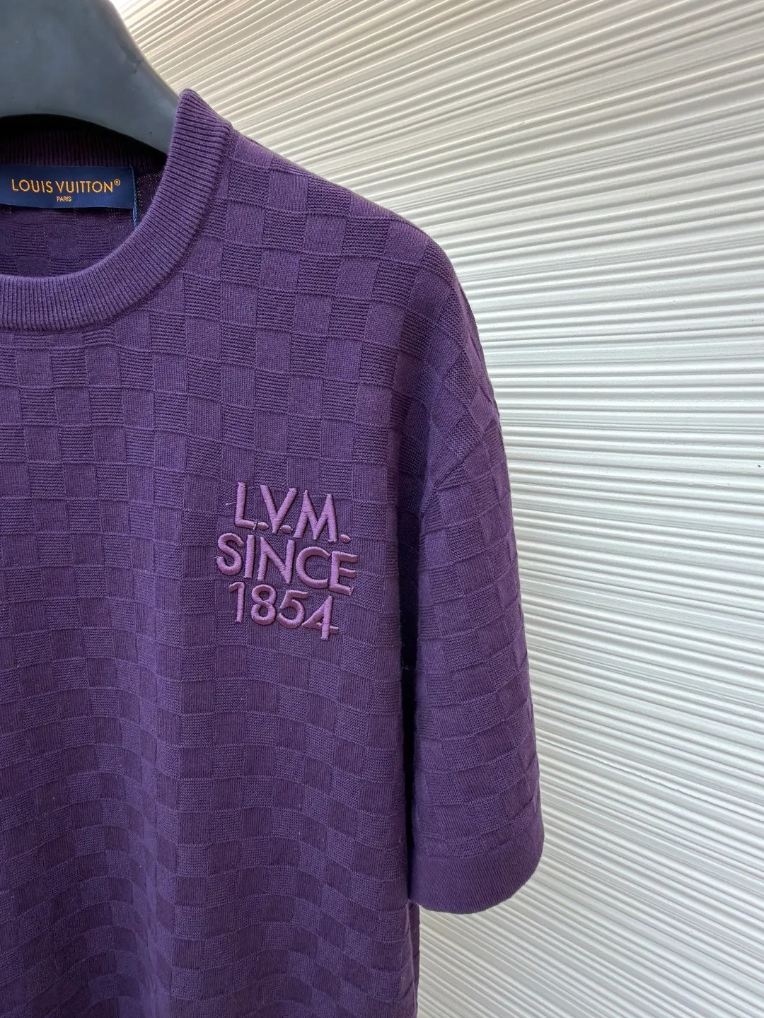 LOUIS VUITTON letter embroidered dark checkerboard jacquard short sleeves ●Original version: Purchased and developed at 9350 ●Item number: 1682319-B00 ●Fabric: 100% cotton ●Technology: jacquard knitting ●Color: Purple ●Version: Fitted version ●Weight: about 340 grams ●Size: S-M-L-XL ●Description: This Louis Vuitton purple knitted short-sleeve is made of custom worsted wool blended fabric. It is created with an 18-needle high-density weaving process using a computerized flat knitting machine to create a three-dimensional checkerboard texture. The checkered pattern is laser positioned and patterned. The size and spacing of each grid are accurate to 0.1 cm, showing a regular relief texture. The left chest uses same-color inlay embroidery technology, and the "LVM SINCE 1854" logo is embroidered with a high density of 1200 stitches/square centimeter. The embroidery thread is made of high-elastic mercerized cotton thread of the same color as the body, forming a natural texture layer with the knitted base. The neckline adopts seamless cylindrical rib technology, which is not easy to loose after high-temperature shaping treatment. The shoulders are made of seamless bonding technology to reduce the abruptness of the seams. The overall micro-profile tailoring combined with the invisible stitching technology of the side seams not only ensures the comfort of wearing, but also makes the body lines smoother. Each process has undergone multiple quality control tests by the brand to ensure the quality and durability of the craftsmanship. The overall wiring is straight and delicate, the fabric is comfortable and soft, and the color is consistent without color difference. It can be matched with the same style to create a fashionable look and control various occasions. Customized accessories, complete with three standards, same style for men and women!